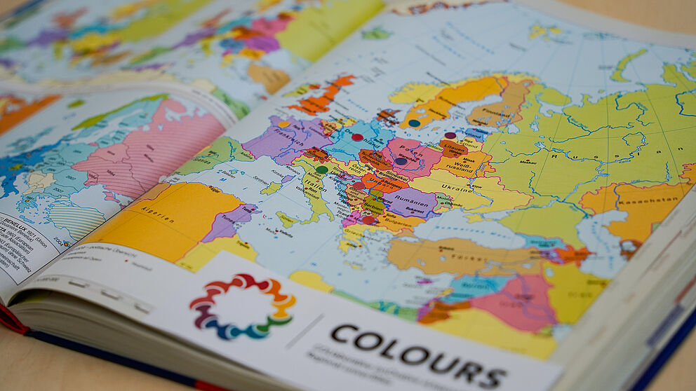 Eine Europa-Karte ist mit bunten Punkten beklebt, die symbolisch fr die Mitgliedsstaaten der Hochschulallianz "COLOURS" stehen. Das Logo der Allianz ist am Bildrand angeschnitten.