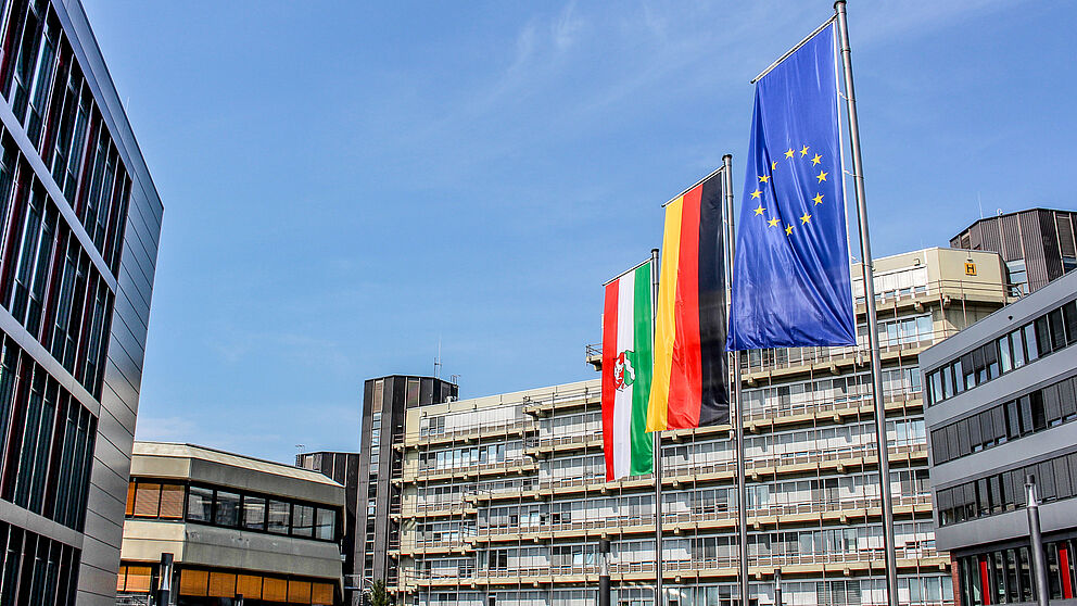 The flag of the state of North Rhine-Westphalia, the flag of Germany and the flag of the European Union are hoisted in front of the main entrance to Paderborn University.