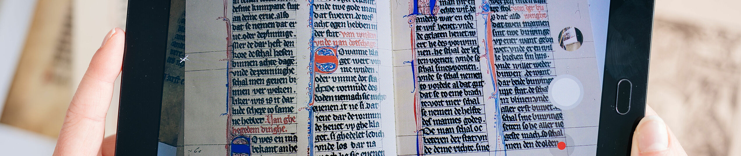 Auf einem beidh?ndig gehaltenen Tablet wird ein Buch mit mittelalterliche Schrift angezeigt